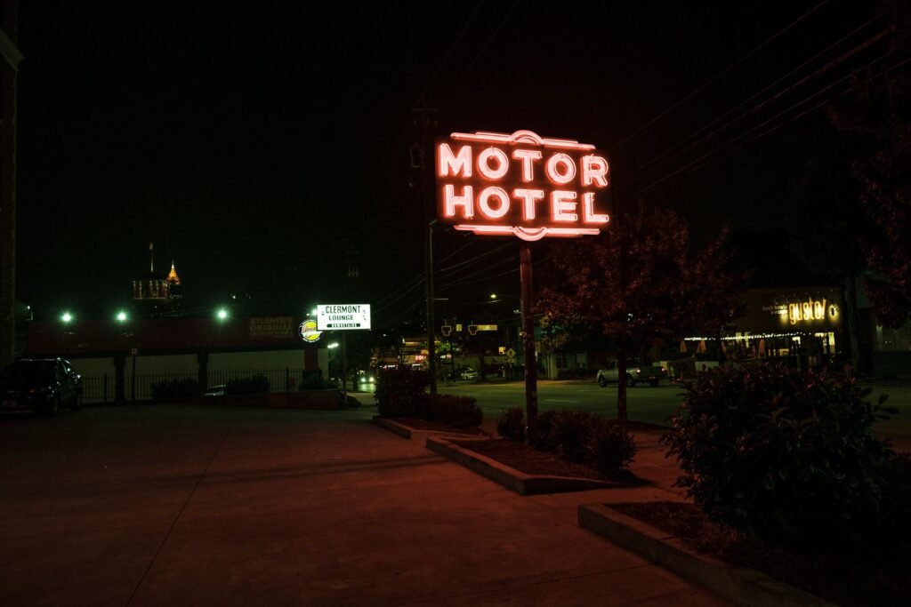 A glowing neon motor hotel sign at night beside a quiet road